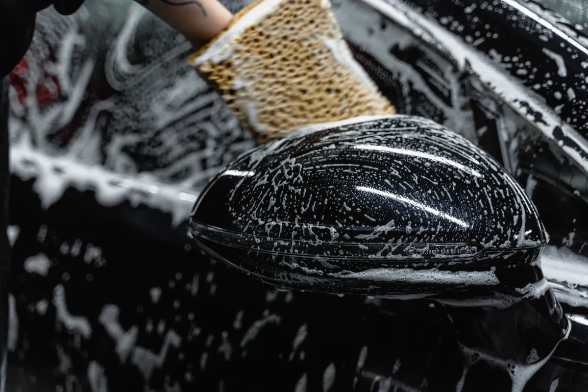 Detailer hand-washing a car panel with foam — the labor hours are what a detail price actually buys