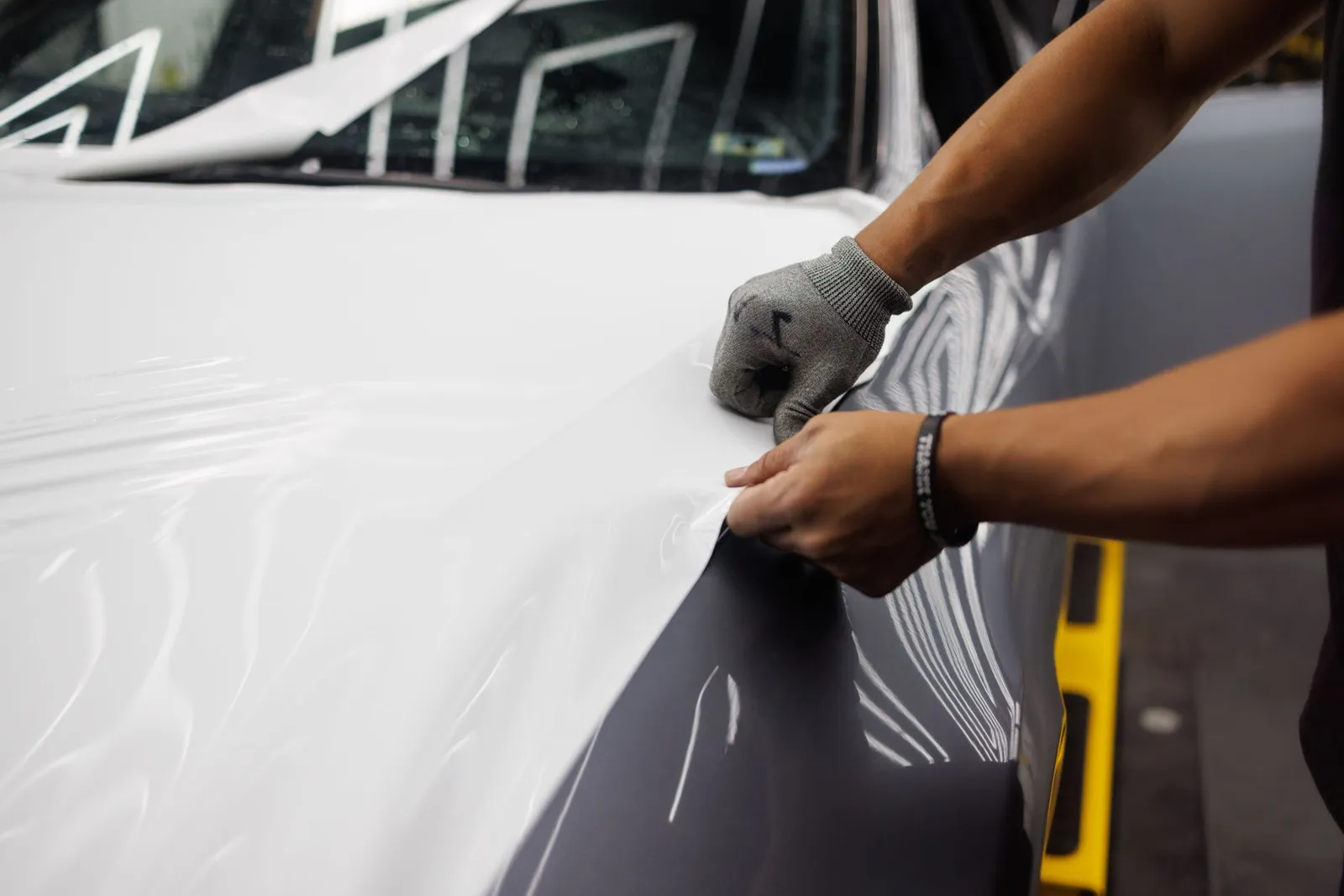 Installer hand-applying protective film to a car hood panel